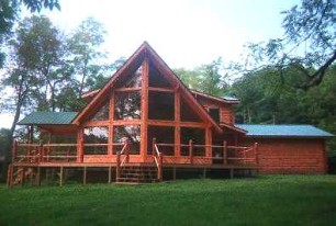 Custom log home with a large covered deck, cedar-colored logs, and a green metal roof