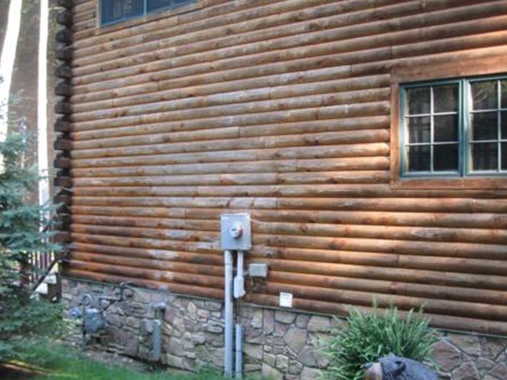Log home wall before restoration, with a darkened, weathered finish and uneven color